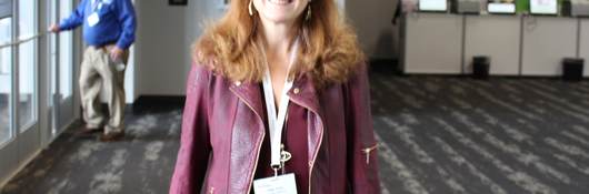 Woman wearing a burgundy jacket with black pants walks around event showroom